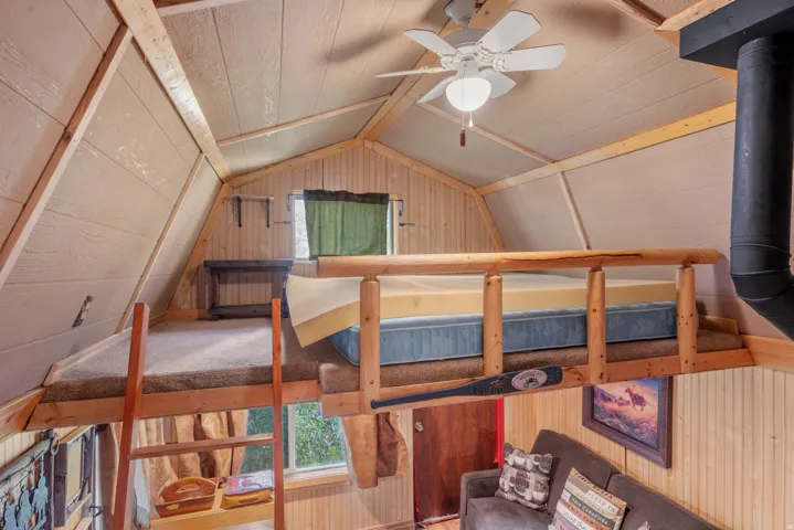 Carpeted loft area with wood railing and sloped wood-paneled walls