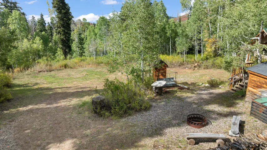 Expansive outdoor area featuring a gravel patio, a metal fire pit, a log bench, and a small log outbuilding