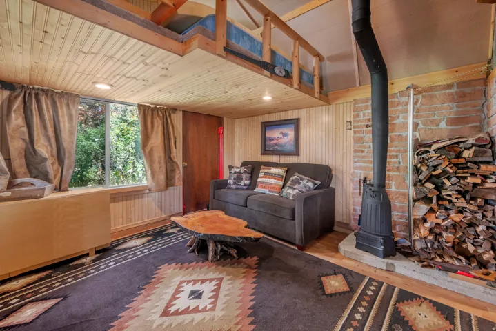 Wood-finish plank ceiling, wood-finish wall paneling, exposed brick wall, wood stove, and a functional loft space