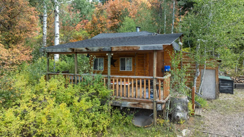 Log cabin exterior featuring a covered porch with wood railings, a dark shingle roof, and a detached storage shed