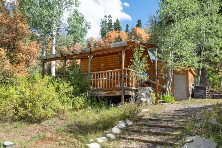 Log cabin exterior featuring a covered porch, wood railing, and an adjacent storage shed