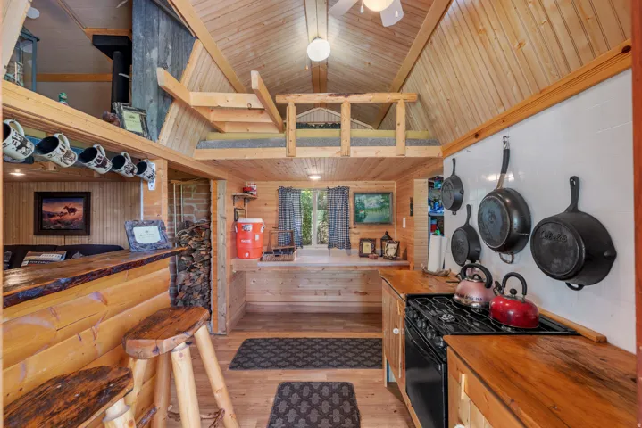 Vaulted wood-paneled ceilings, wood-finish flooring, a functional kitchen with a built-in range, a wood-slab countertop bar, and an overhead loft space