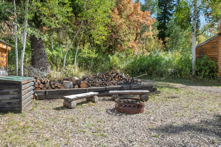 Gravel yard featuring a fire pit, two log benches, and a wood storage area with stacked logs