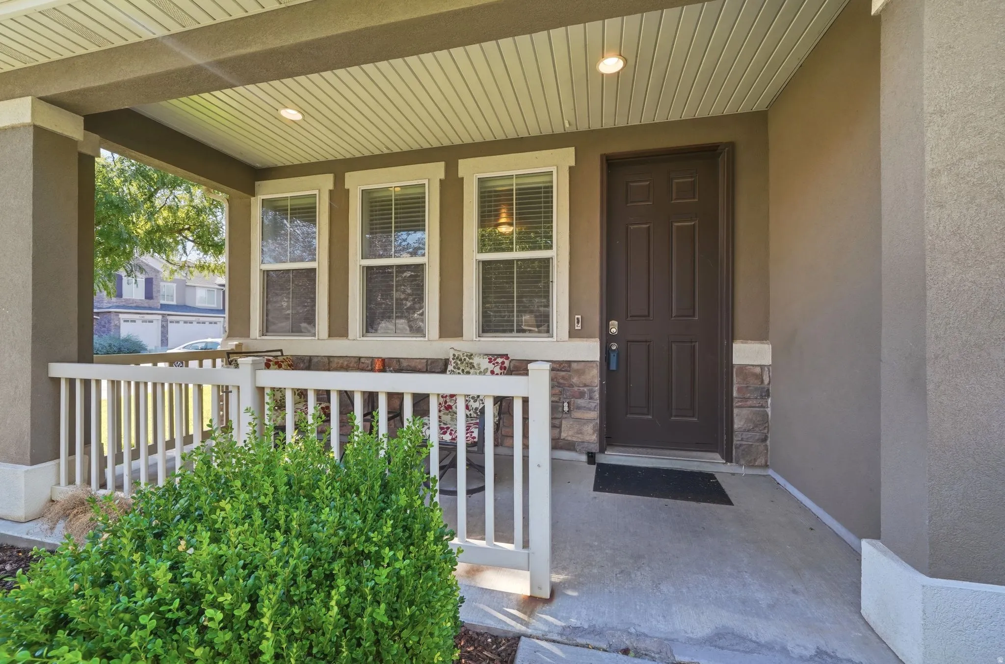 Covered front porch featuring recessed lighting, a paneled entry door, stone veneer accents, and a white picket railing