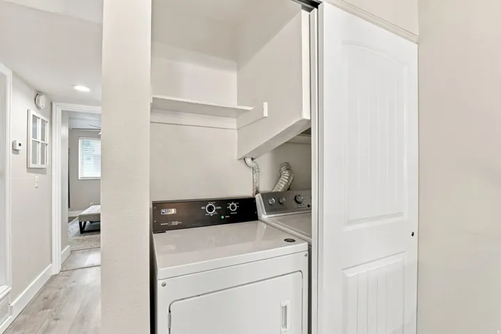 Stackable washer and dryer unit with overhead shelving, contained within a white paneled sliding door closet