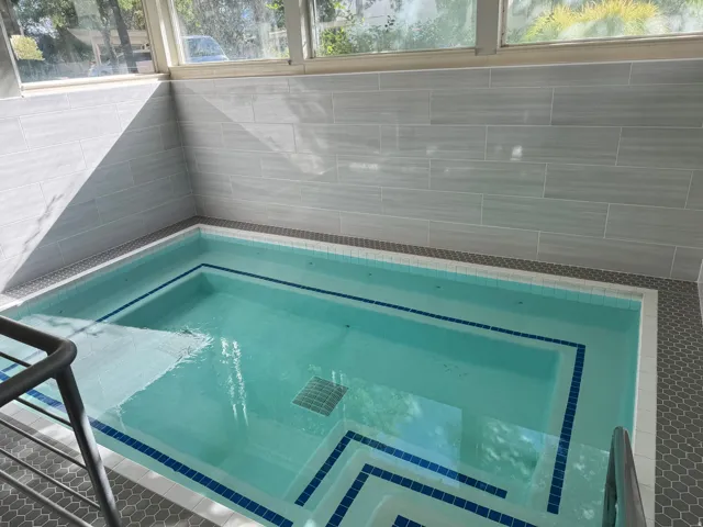 Indoor pool with light blue water, integrated steps, and a metal handrail