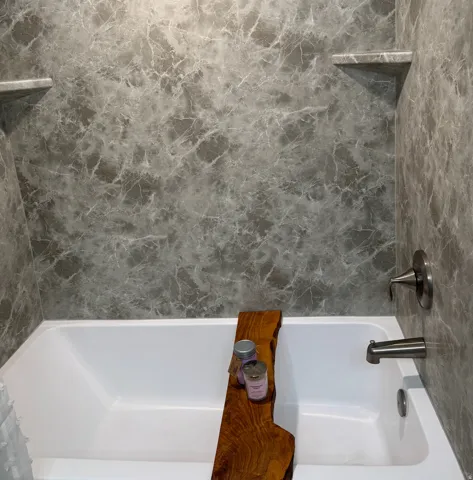 White bathtub with grey marbled-patterned surround and two integrated corner shelves