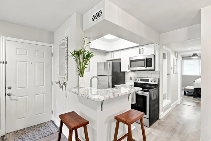 Kitchen with white cabinetry, stainless steel appliances, white subway tile backsplash, and light-toned countertop with breakfast bar seating