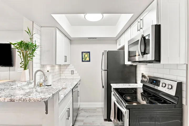 Kitchen featuring white shaker-style cabinetry, granite-finish countertops, stainless steel appliances, and subway tile backsplash