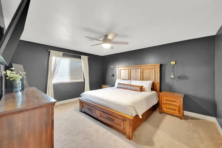 Carpeted flooring, ceiling fan with integrated lighting, window with blinds and drapes, and built-in wall sconces