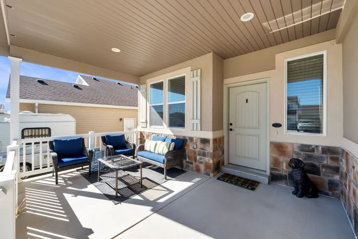 Covered front porch with concrete flooring, stone veneer accents, and decorative shutters