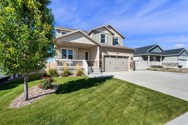 Exterior featuring a front porch with white railing, stone accents, two-car garage, and a concrete driveway