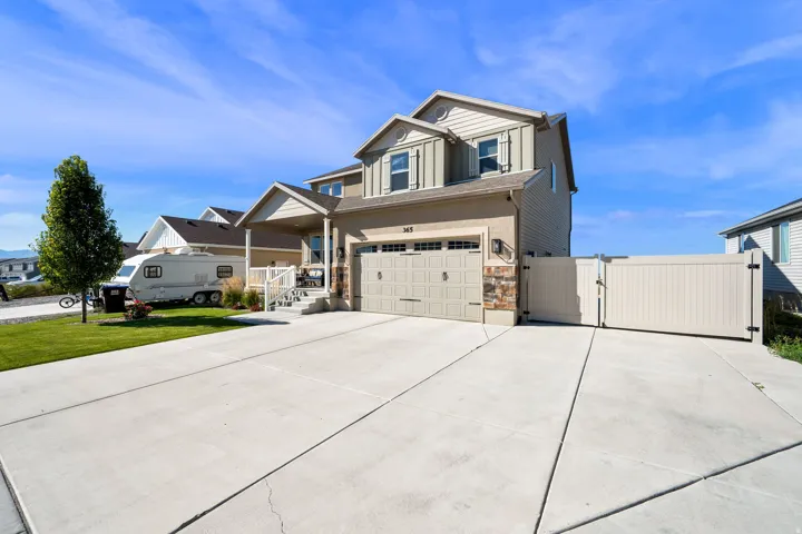 Two-story exterior with siding and stone accents, featuring a two-car garage, a concrete driveway, and a gated side yard