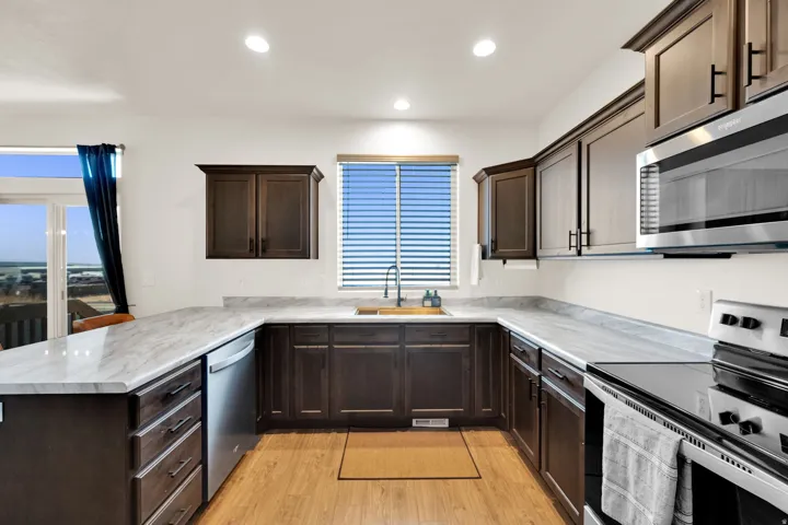 Kitchen featuring extensive counter space, wood-finish flooring, dark wood cabinetry, a stainless steel dishwasher, and a built-in microwave