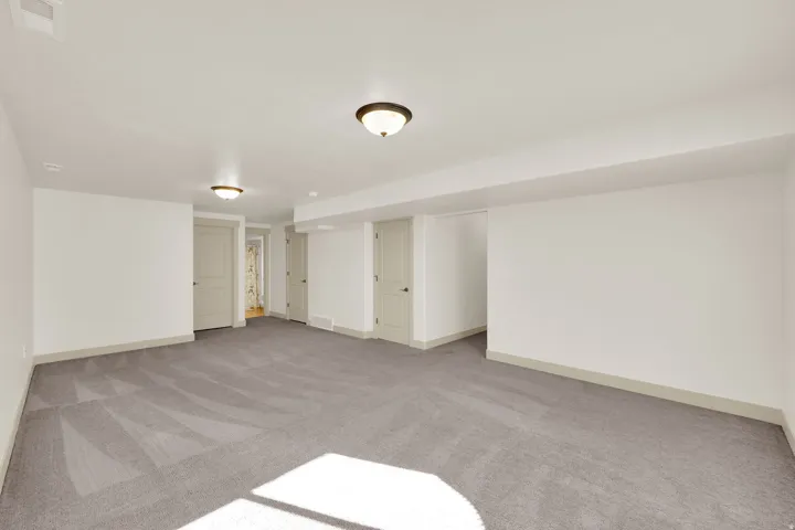 Spacious room with gray carpeting, white walls, multiple entryways, and flush-mount ceiling lighting