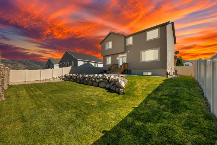 Expansive backyard featuring a manicured lawn, a rock retaining wall, and a vinyl privacy fence
