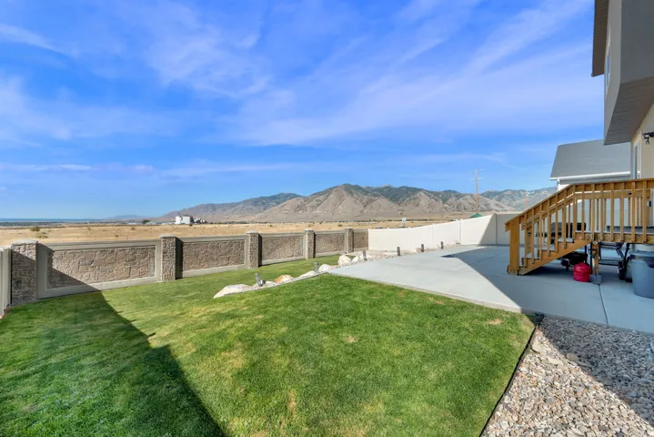 Expansive backyard featuring a concrete patio, wood deck with stairs, and a decorative stone-look perimeter fence