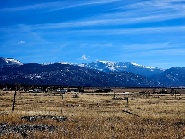 Expansive open field with scattered fencing, set against a backdrop of snow-capped mountains and a clear blue sky