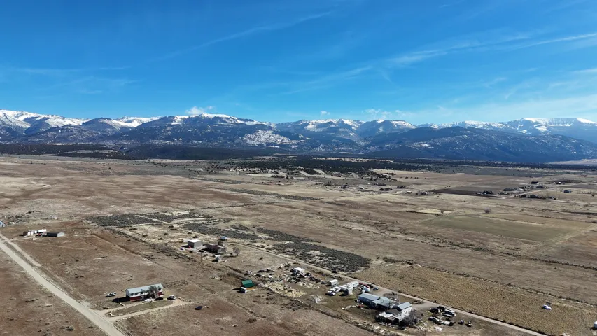 Expansive rural landscape featuring a distant mountain range with snow-capped peaks, scattered individual buildings, and unpaved roadways