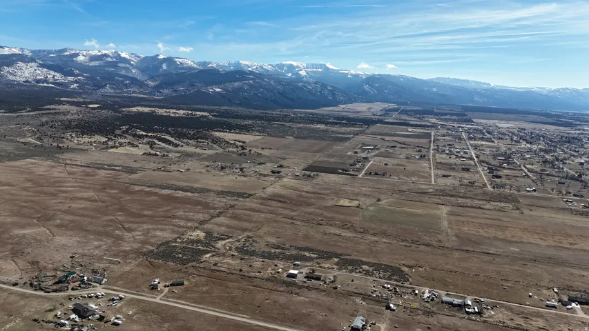 Expansive rural landscape featuring a distant town, surrounding open land, and snow-capped mountains on the horizon