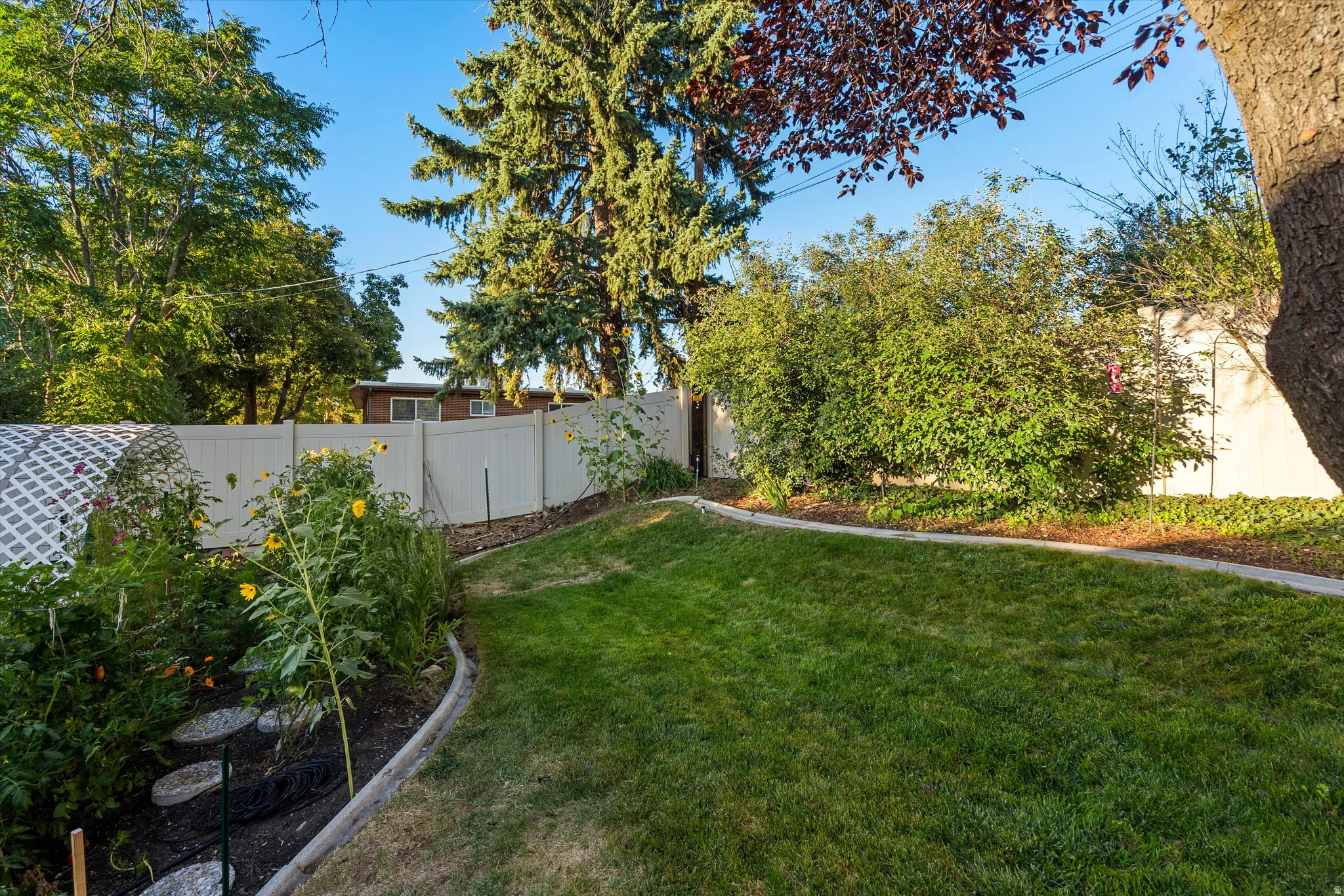 Fenced backyard featuring a manicured lawn, established landscaping, and a garden bed