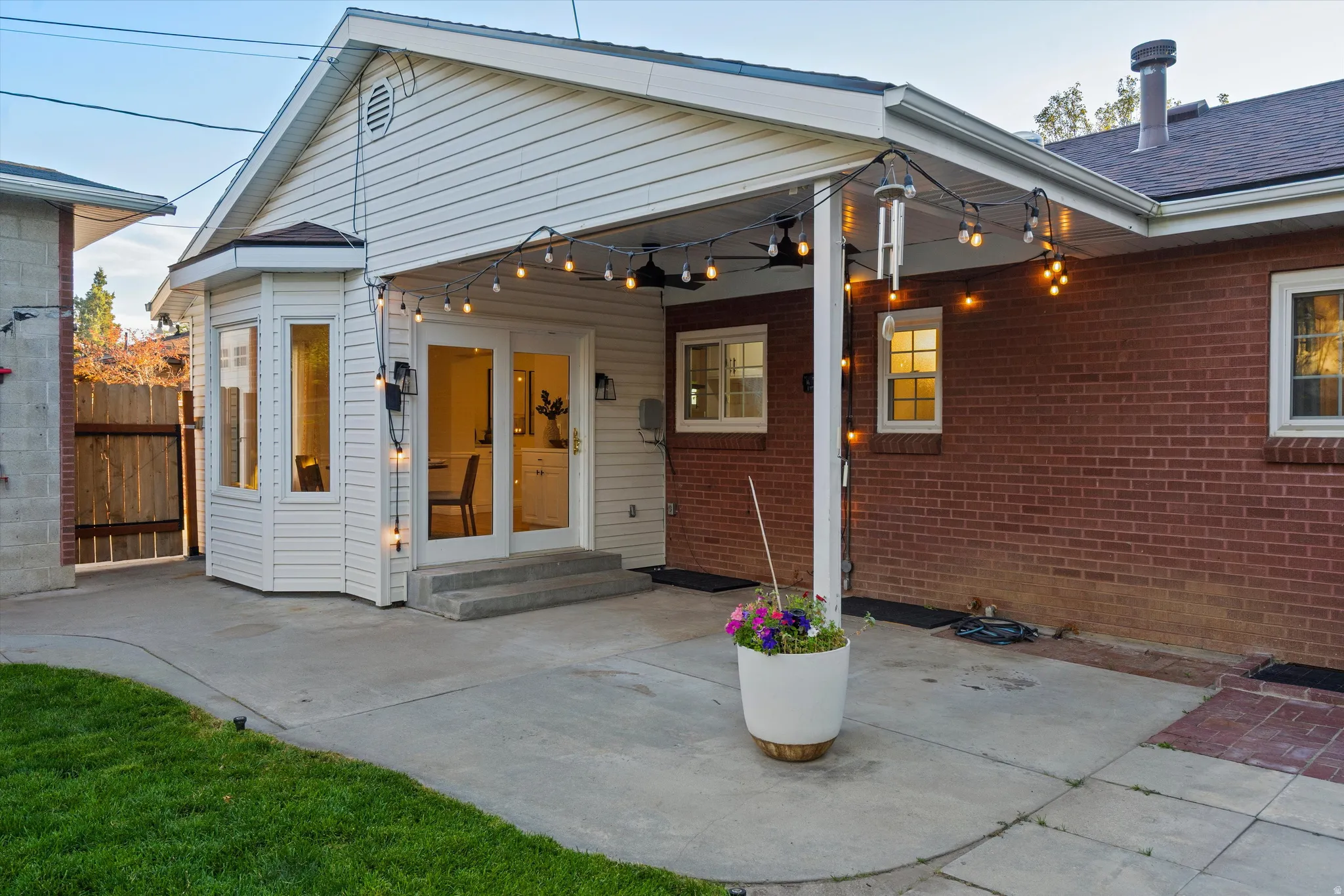 Expansive concrete patio with covered awning, bay window, white siding, and exposed brick exterior