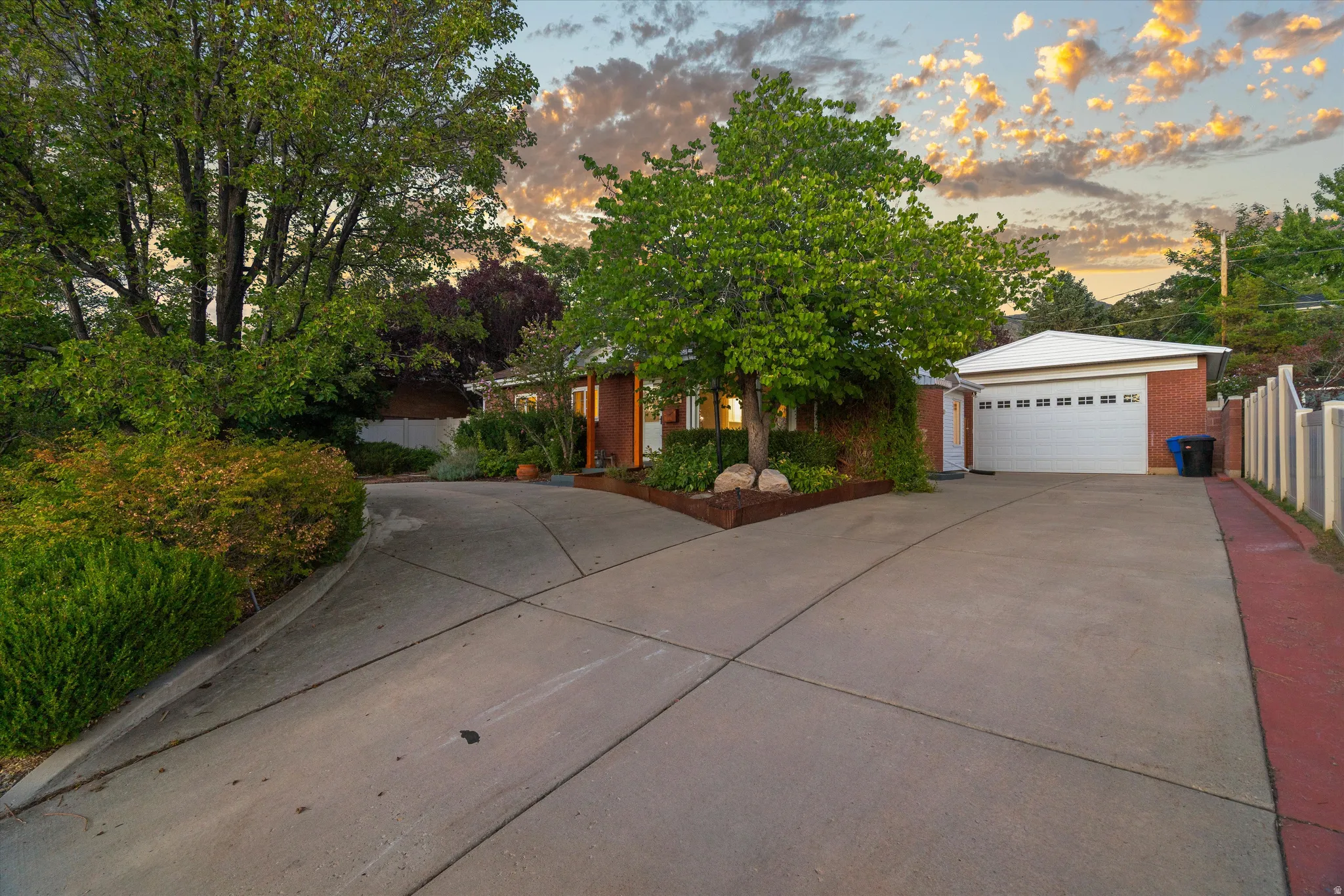 Brick exterior with a two-car garage, concrete driveway, and mature landscaping