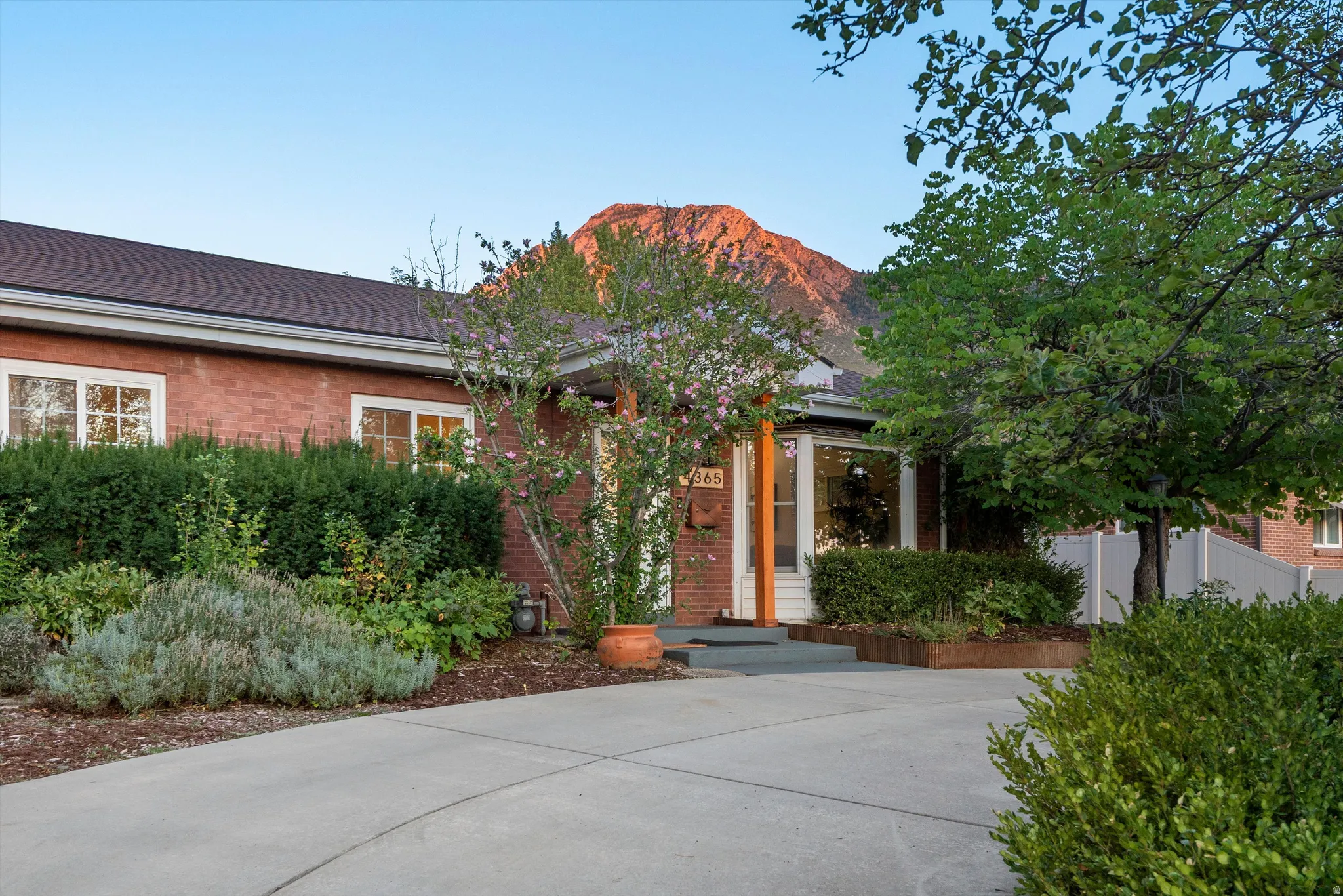 Brick exterior with white-framed windows, surrounded by mature landscaping and a paved driveway
