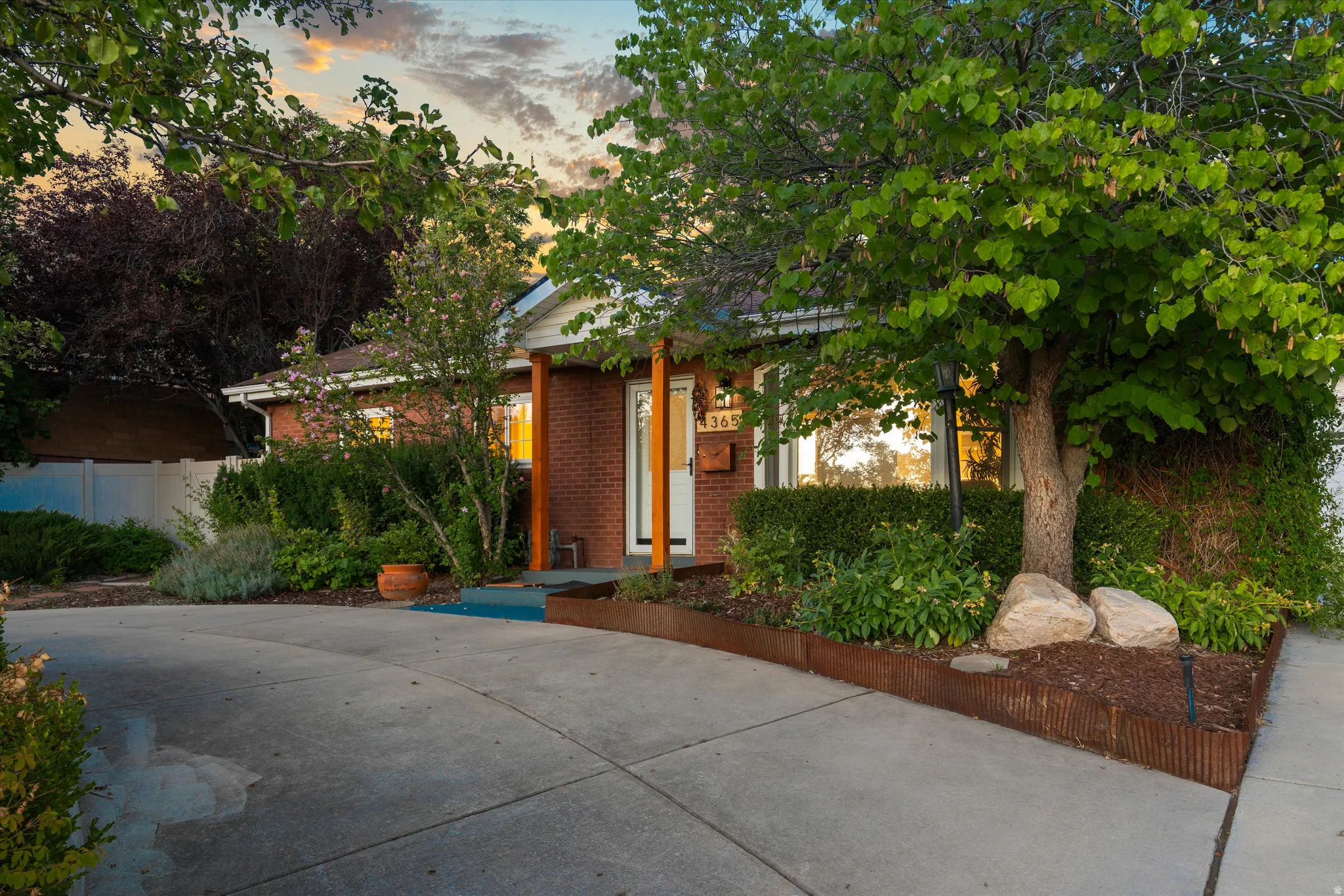Brick exterior with white trim, featuring a mature tree and established landscaping