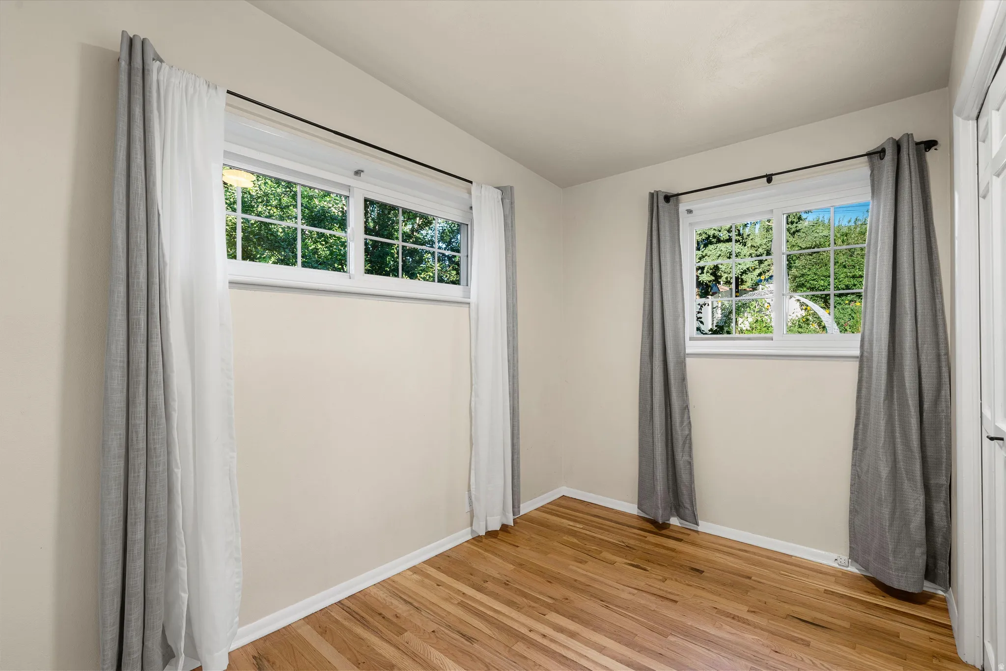 Bedroom #2 Hardwood flooring, two large windows, white trim, and a white paneled door