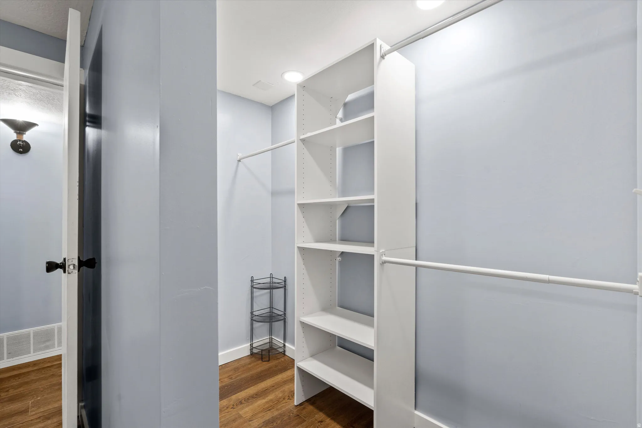 Walk in closet in room #4  Built-in shelving, hanging rods, recessed lighting, and wood-finish flooring