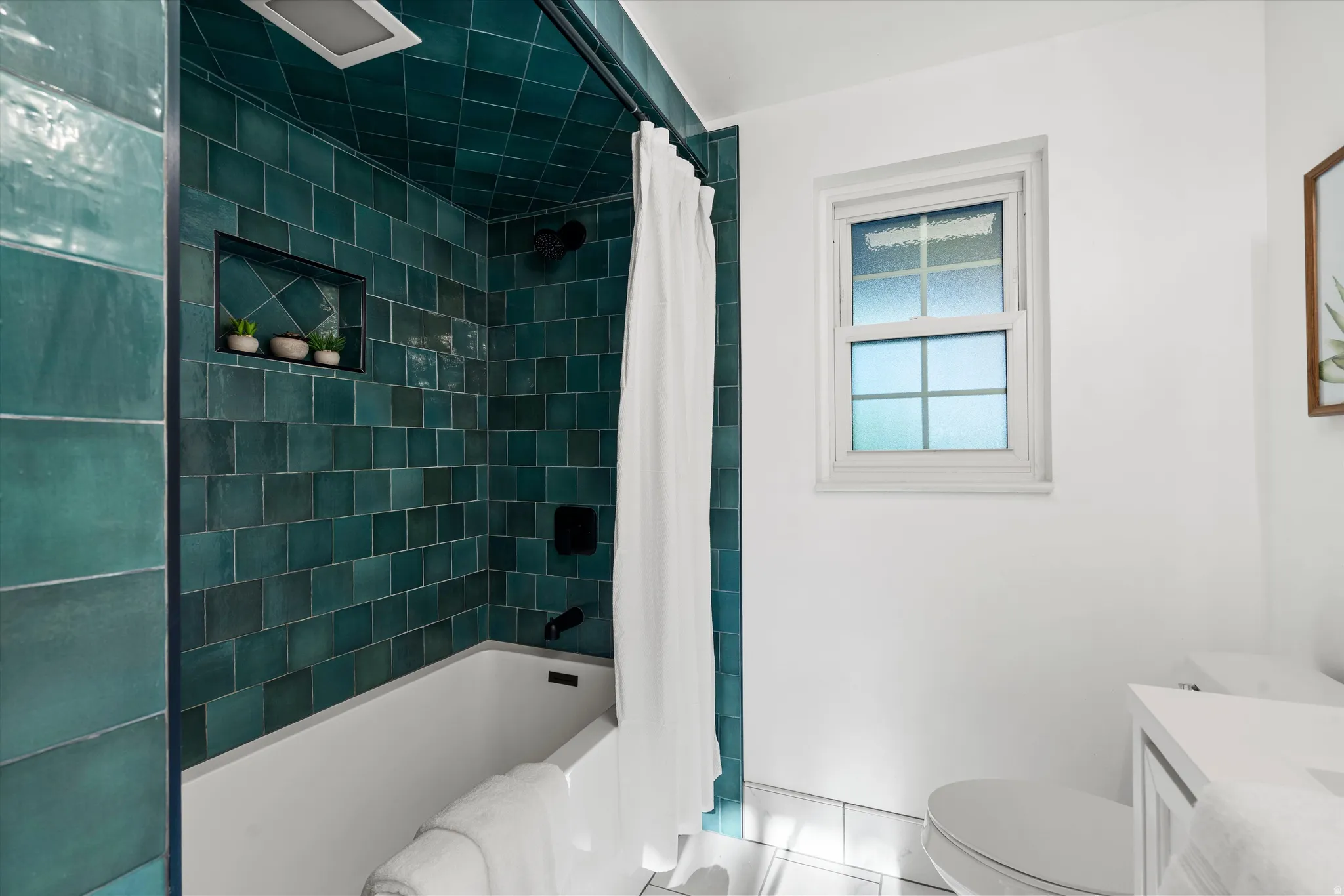 Full bath #1  featuring a white tub, teal subway tile shower surround with integrated niche, and a window with frosted glass