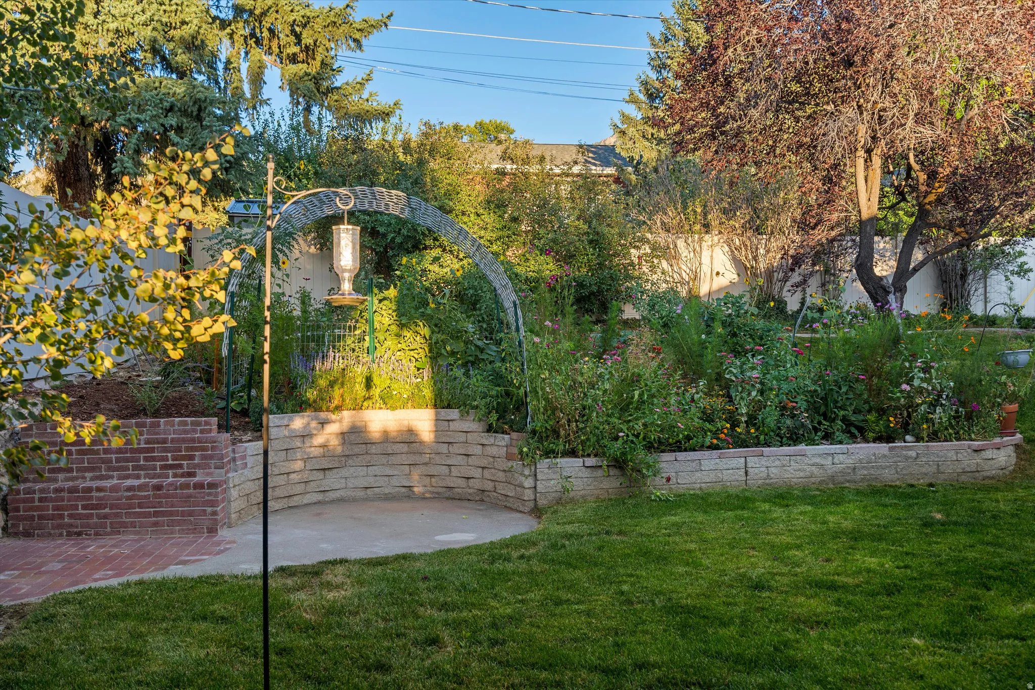 Landscaped garden area featuring a brick patio, stone block retaining wall, and a decorative metal arch