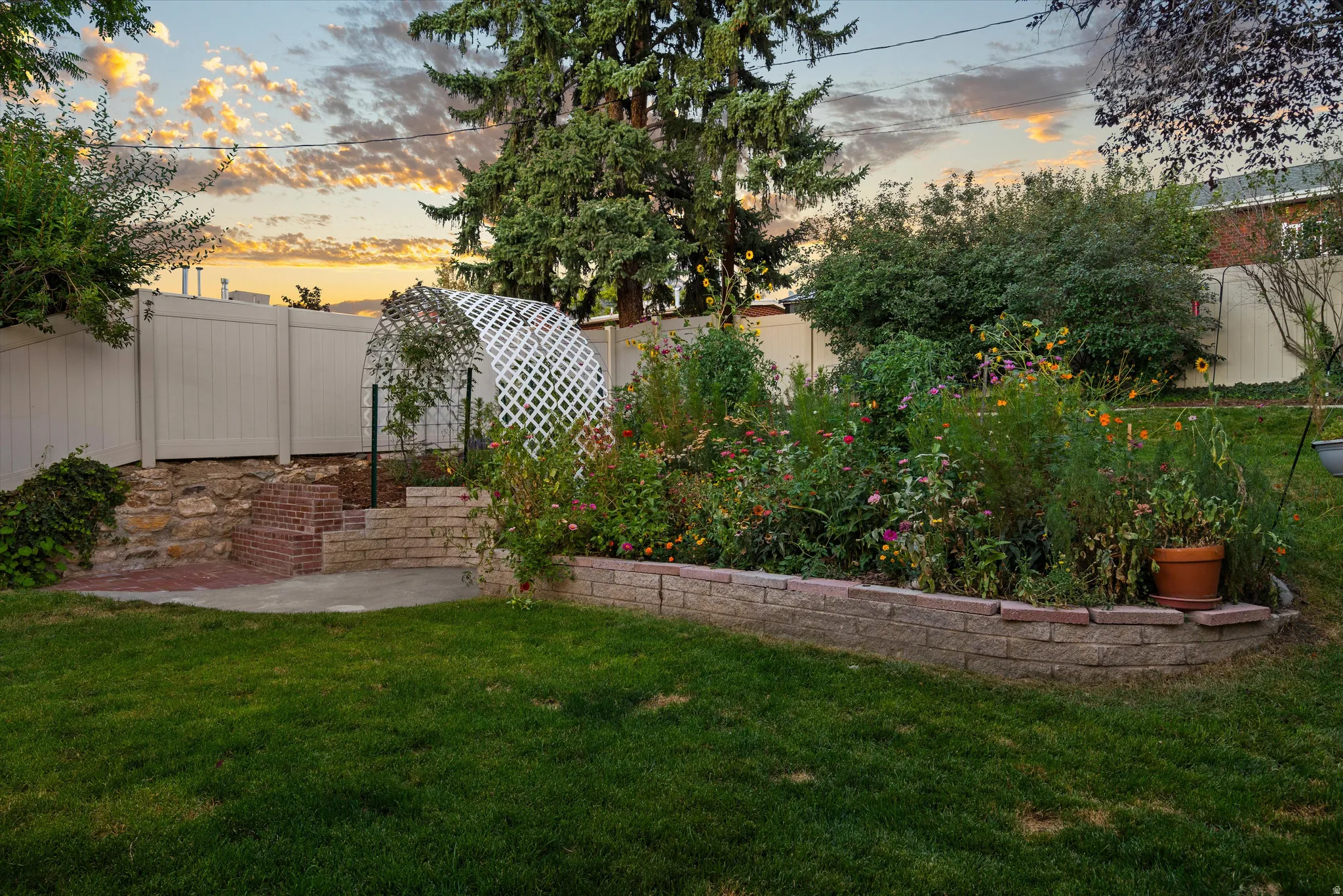 Expansive green lawn with a raised garden bed, stone retaining wall, and a white lattice archway