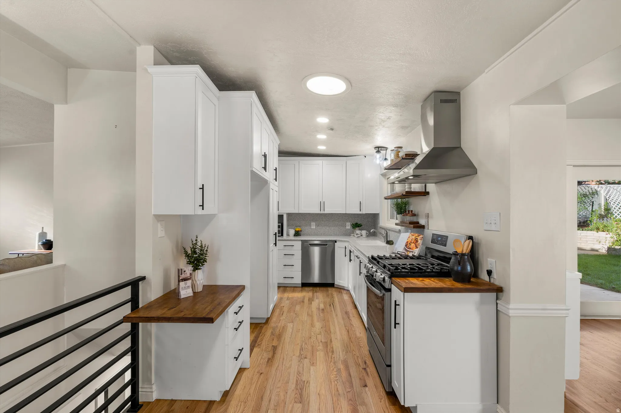 Galley kitchen featuring white cabinetry, wood-finish flooring, stainless steel appliances, with butcher block countertop accents
