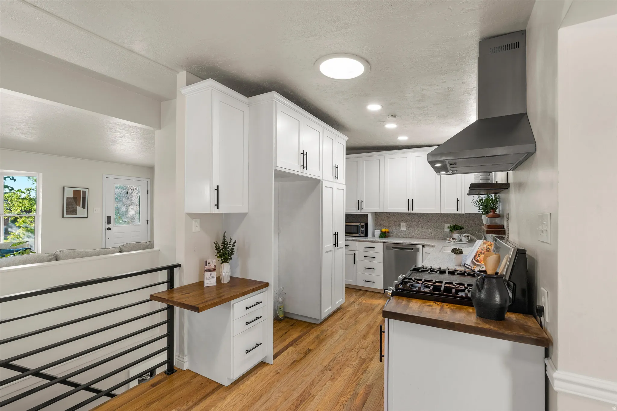 White cabinetry with matte black hardware, wood-finish flooring, a stainless steel range hood, built-in range, and a built-in folding countertop