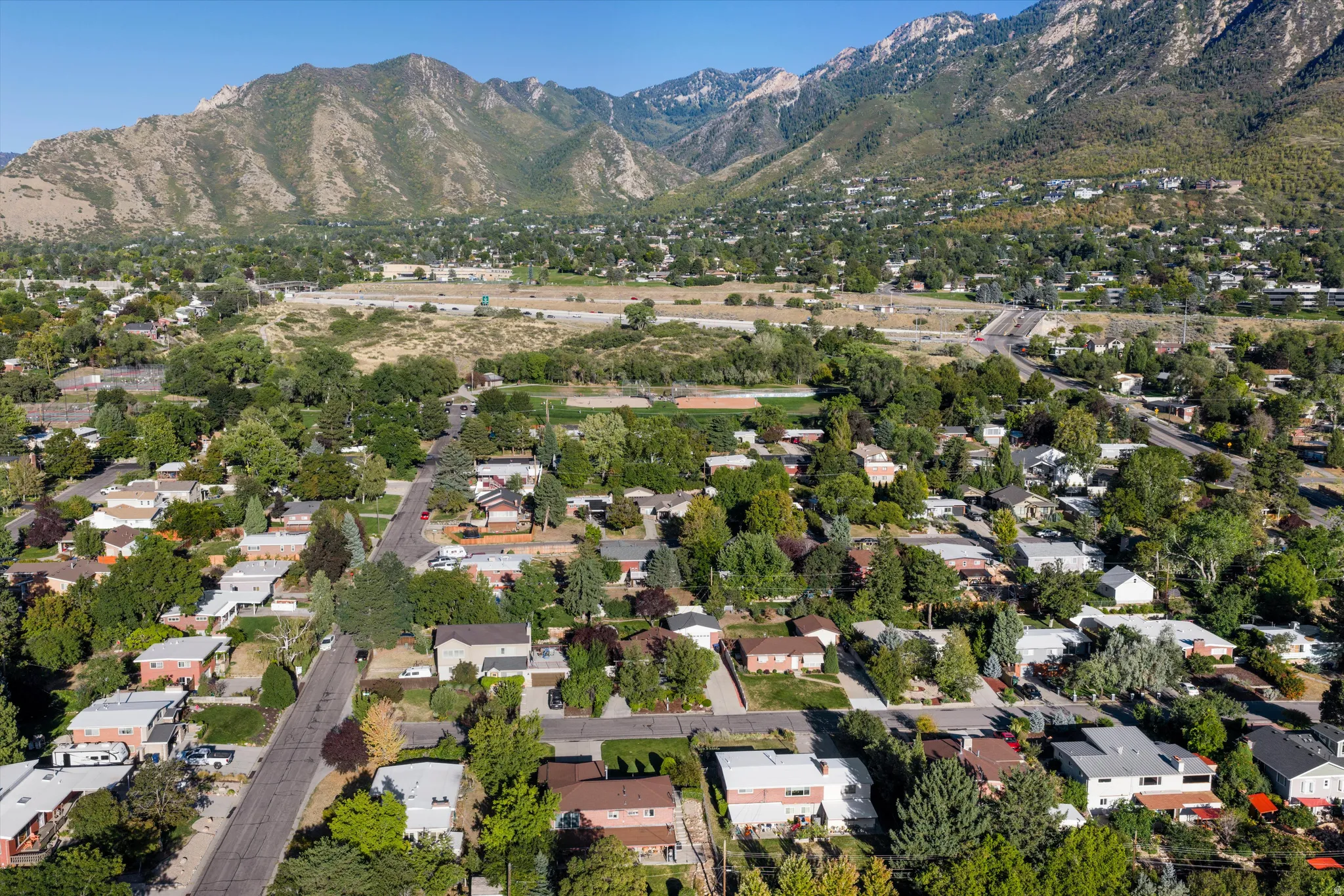 Expansive aerial perspective showcasing a residential area with mature trees, established streets, and mountain ranges in the background