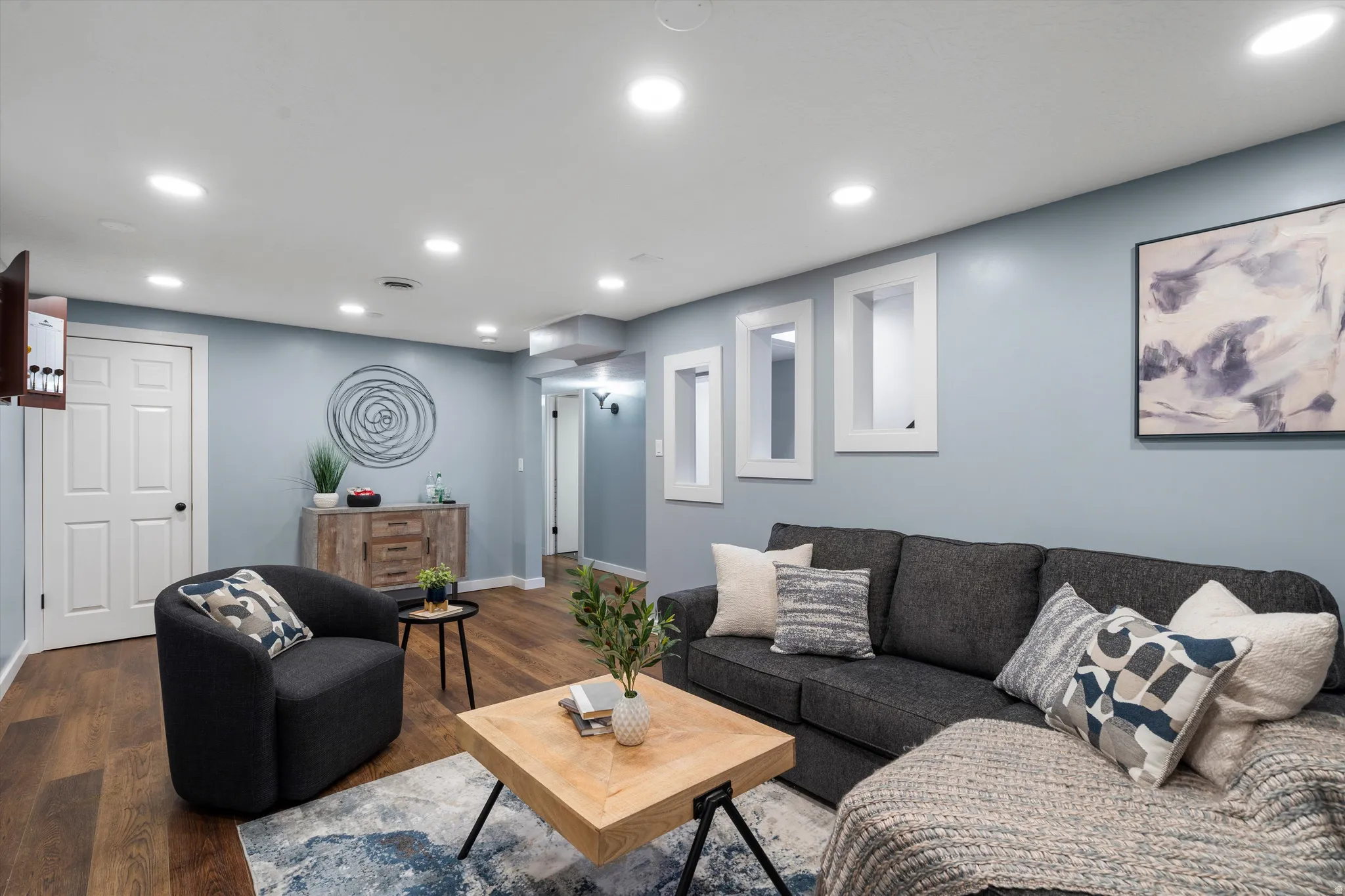 Recessed lighting illuminating the space, featuring three wall niches, wood-finish flooring, and a white paneled door
