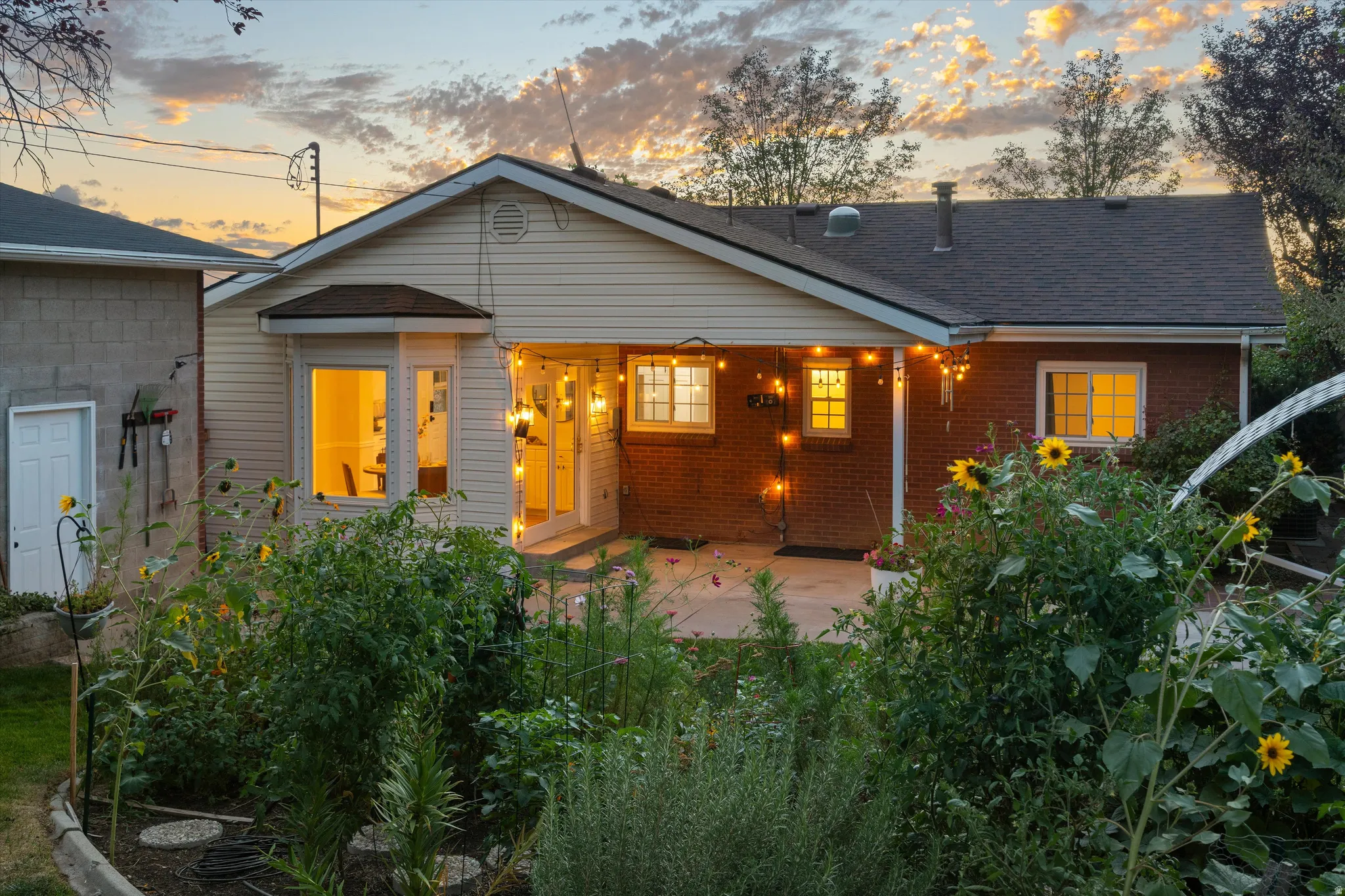 Rear brick and siding exterior with a covered patio, garden beds, and a bay window