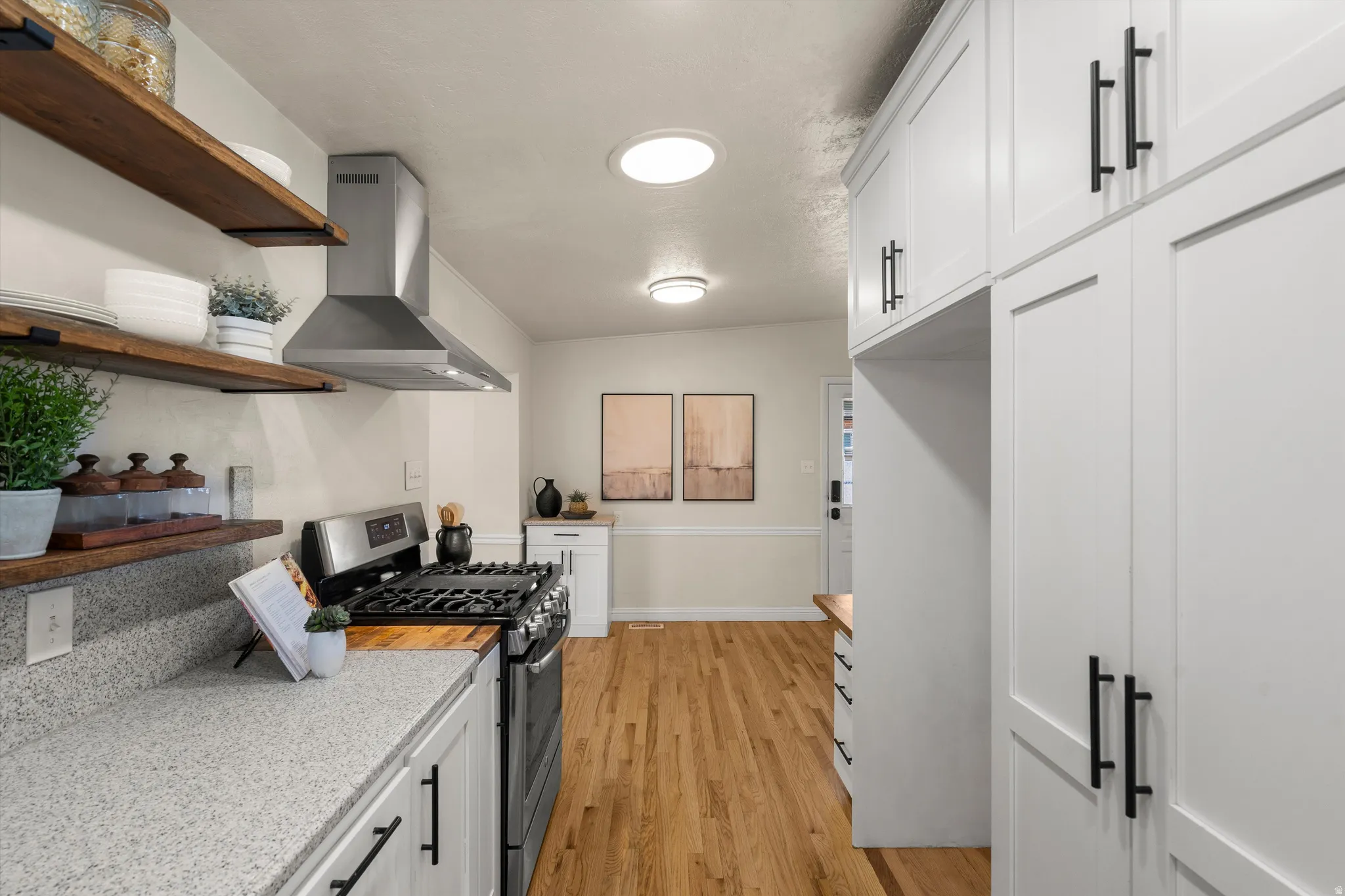 White shaker cabinetry with matte black hardware, stainless steel gas range, hardwood flooring, open shelving, and granite-finish countertops