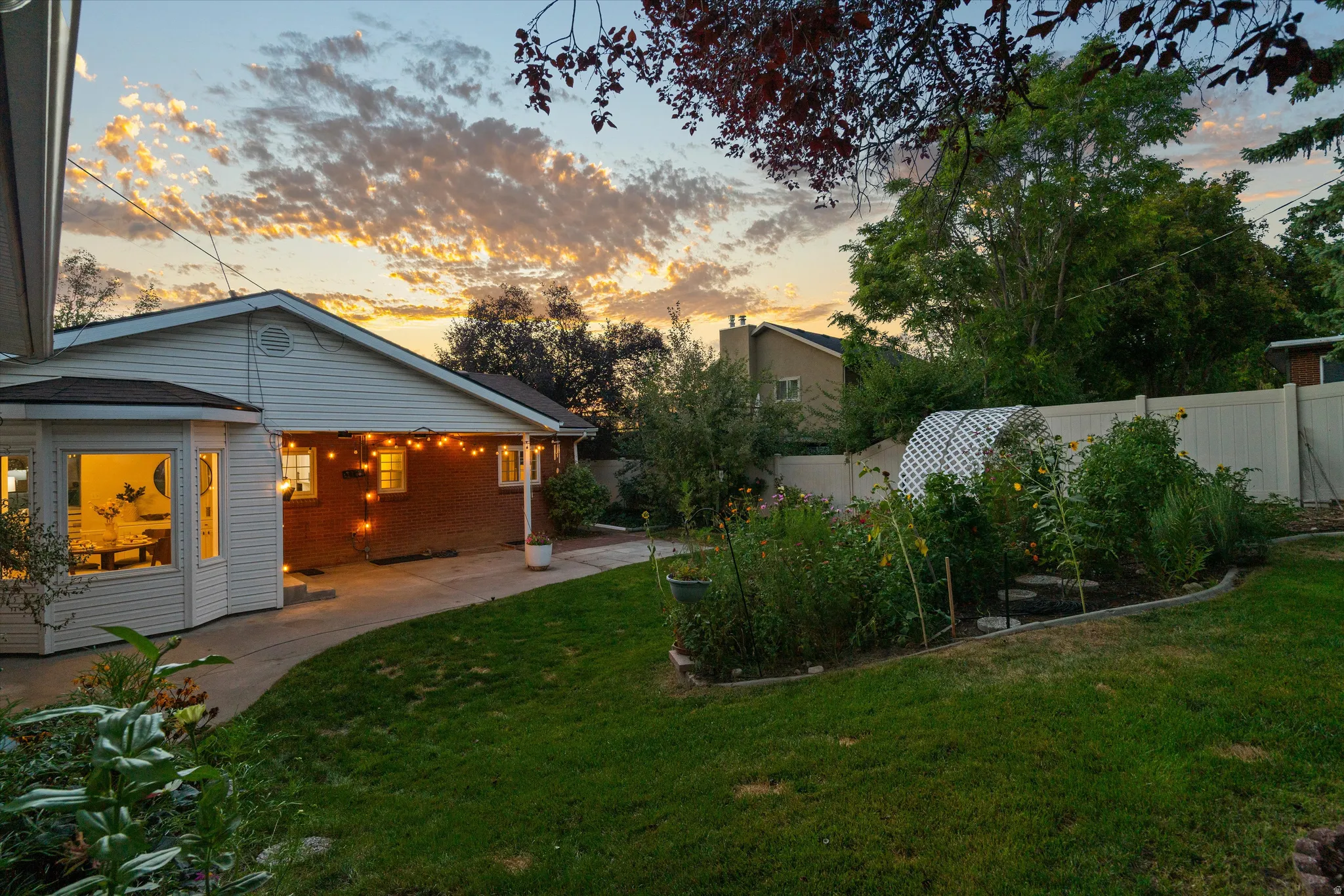 Backyard featuring a bay window, established garden beds, and a white privacy fence