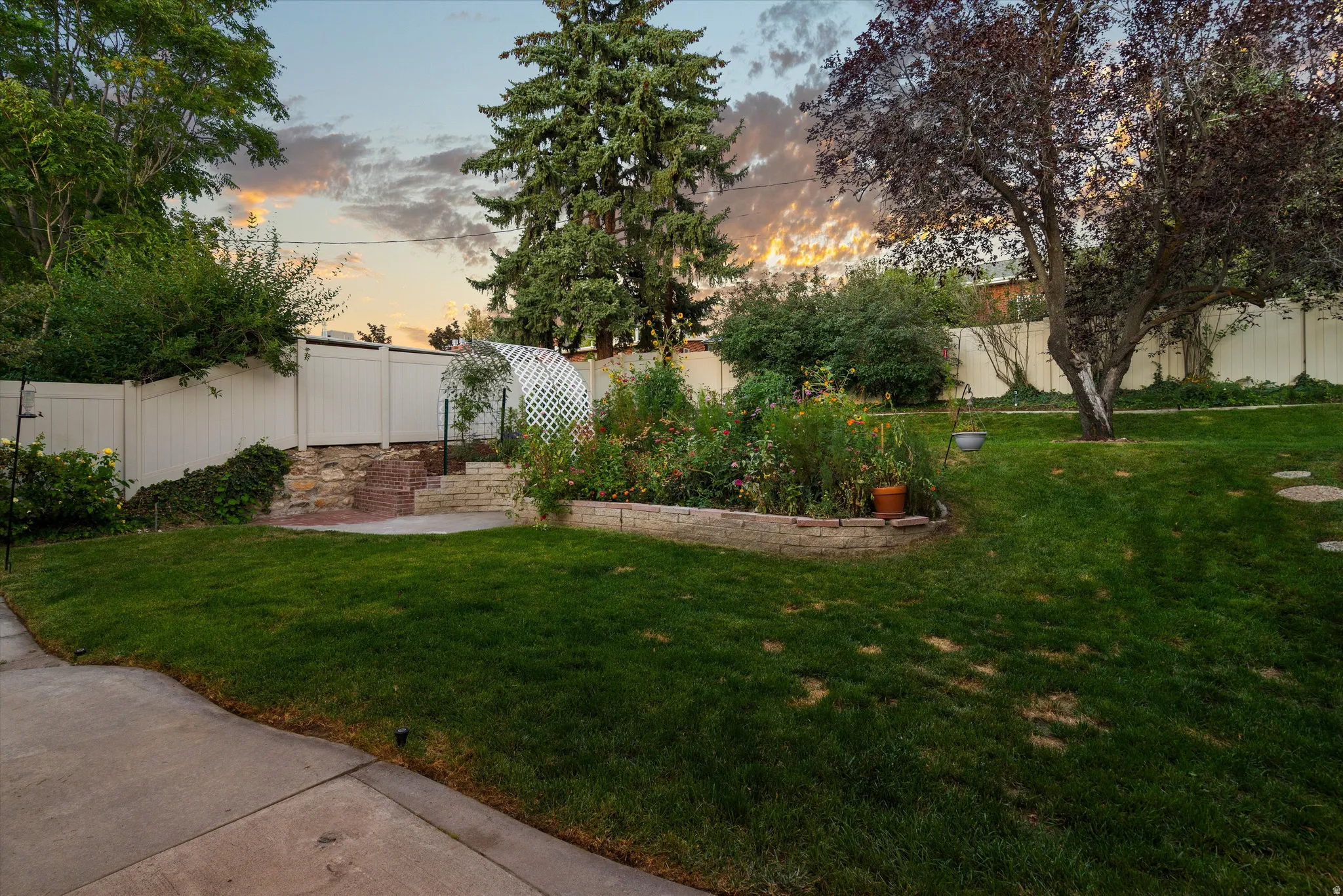 Expansive yard featuring a manicured lawn, established landscaping, privacy fencing, a tiered patio, and a garden area with a lattice arch
