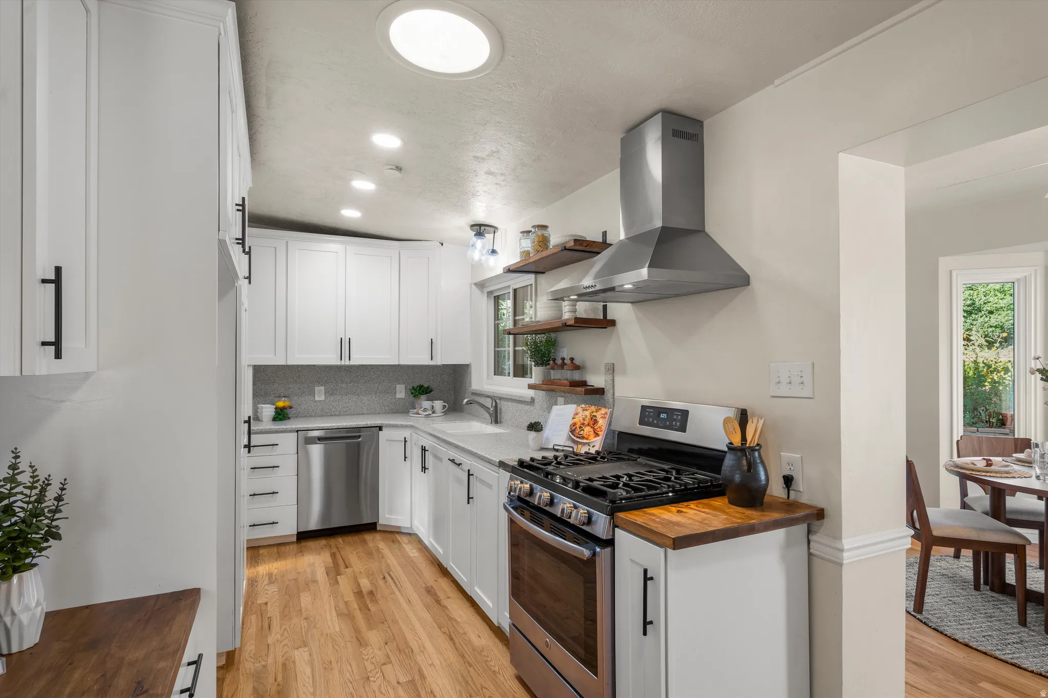 Galley kitchen featuring white cabinetry, wood-finish flooring, stainless steel appliances, with butcher block countertop accents