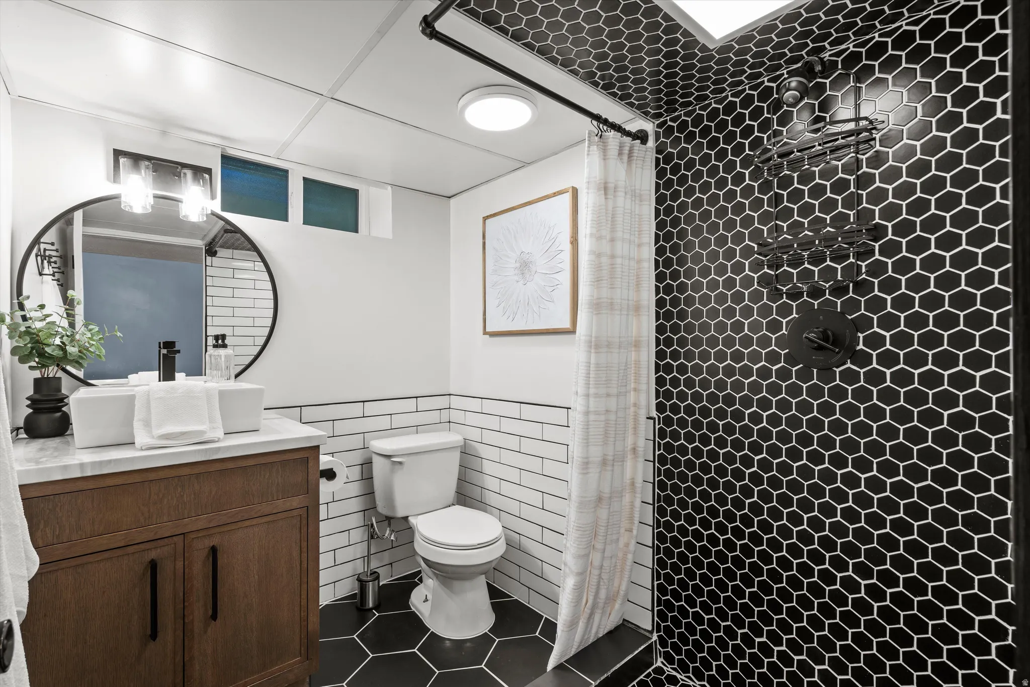 Bathroom #2 featuring a dark wood-finish vanity with a vessel sink, a circular mirror, and a black hexagonal tiled shower with a matte black shower system