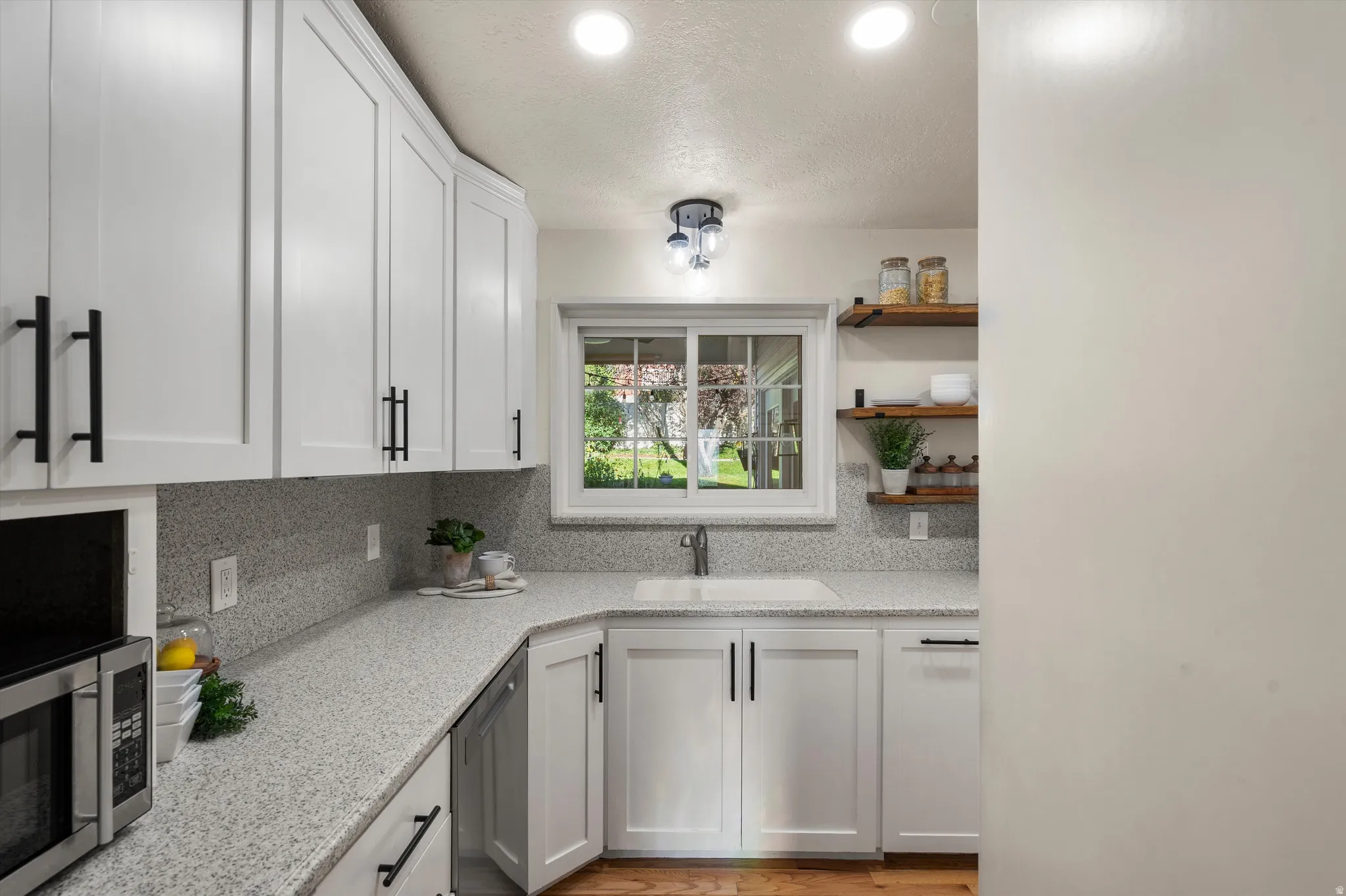 White shaker-style cabinetry with black hardware, light-toned countertop, and matching backsplash