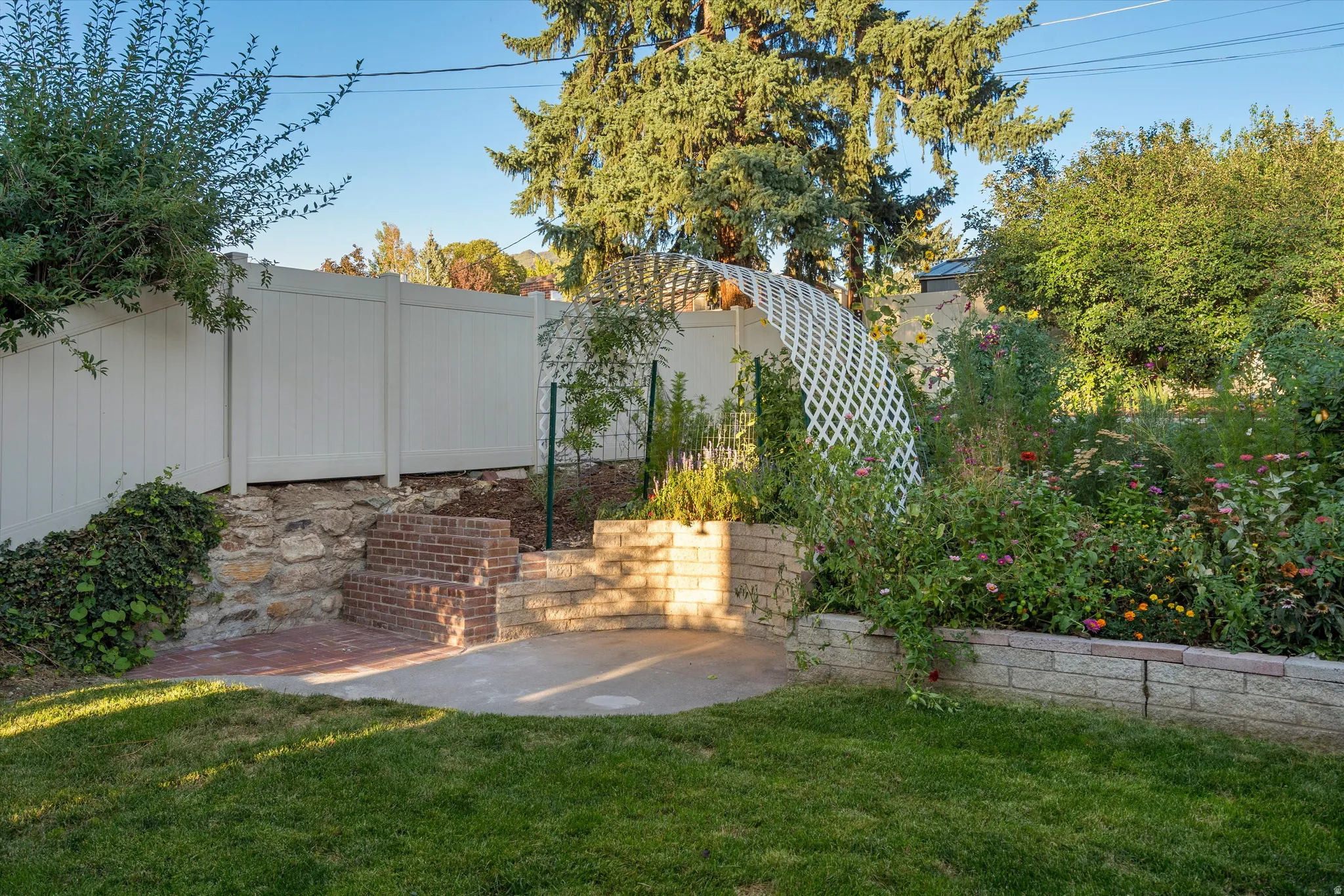 Expansive backyard featuring a manicured lawn, white privacy fencing, a brick retaining wall, and a decorative garden archway