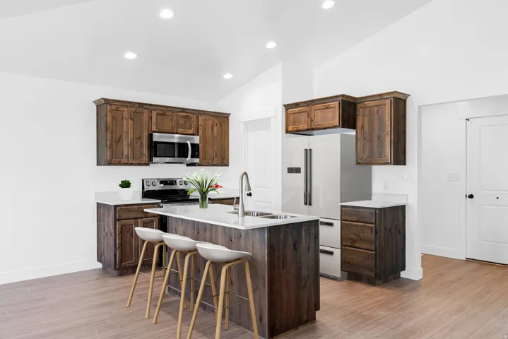 Kitchen featuring wood-finish cabinetry, stainless steel appliances, a center island with sink, and white countertops