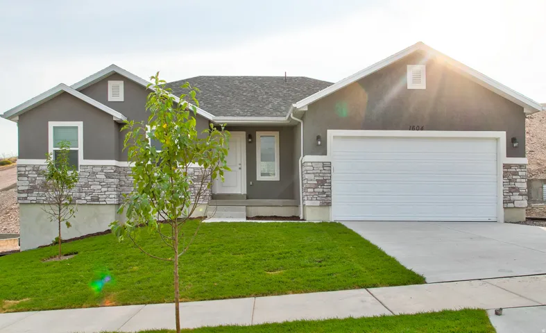 Stucco exterior with stone accenting, an attached two-car garage, a concrete driveway, and a manicured lawn