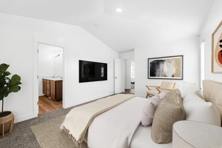 Vaulted ceiling, recessed lighting, white walls, carpeted flooring, and a doorway to an adjacent bathroom