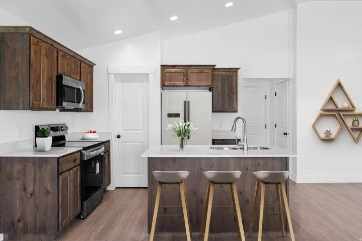 Kitchen featuring dark wood-finish cabinetry, light-toned countertops, stainless steel appliances, and an island with an integrated sink
